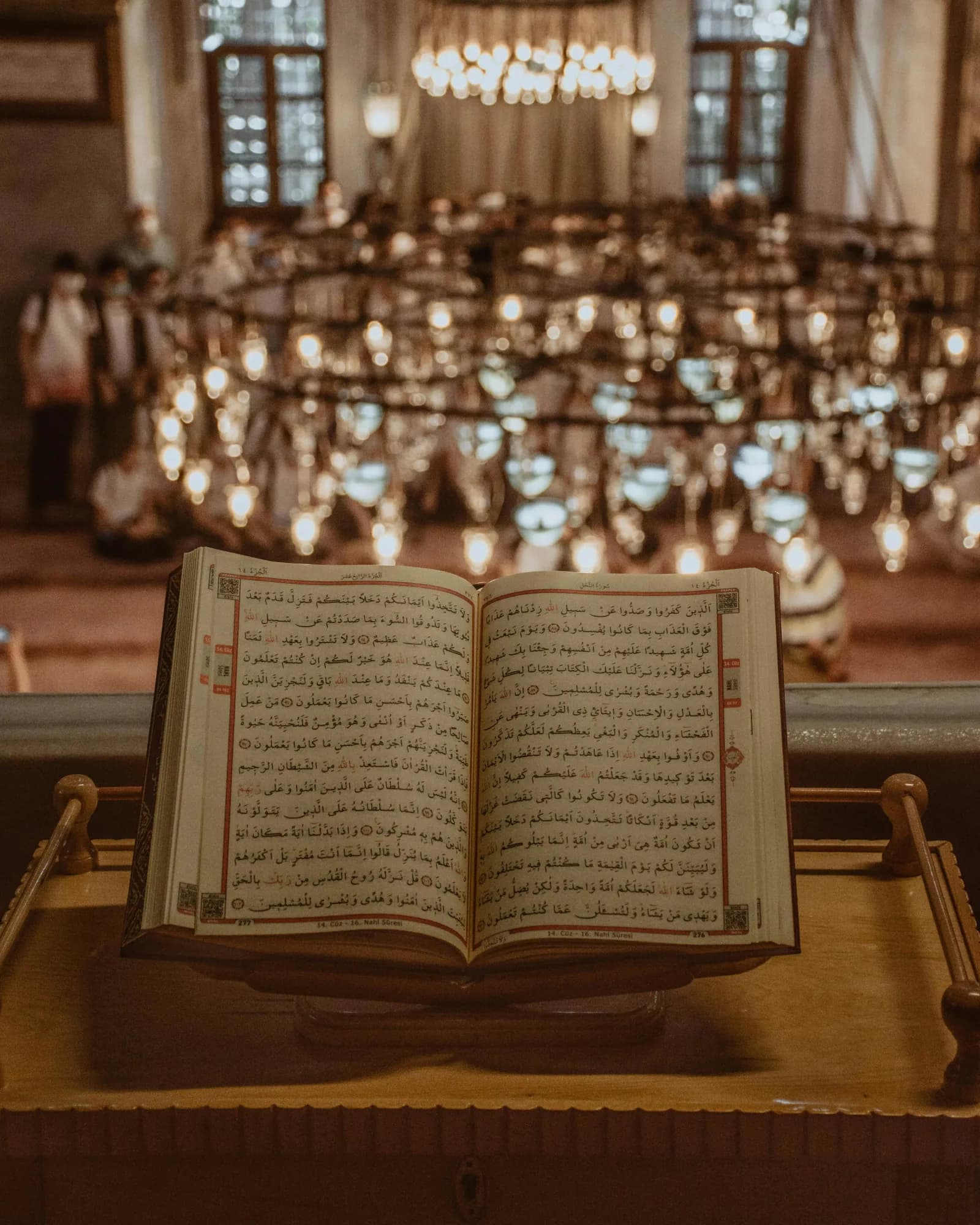 An open Quran resting on a wooden stand beneath mosque lamps